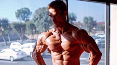 Mike O'Hearn poses shirtless in front of a window.