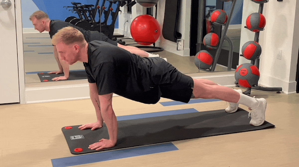 Man wearing a black shirt and shorts performs mountain climbers on a yoga mat.