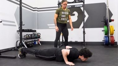 A person doing push-ups and being guided by an expert.