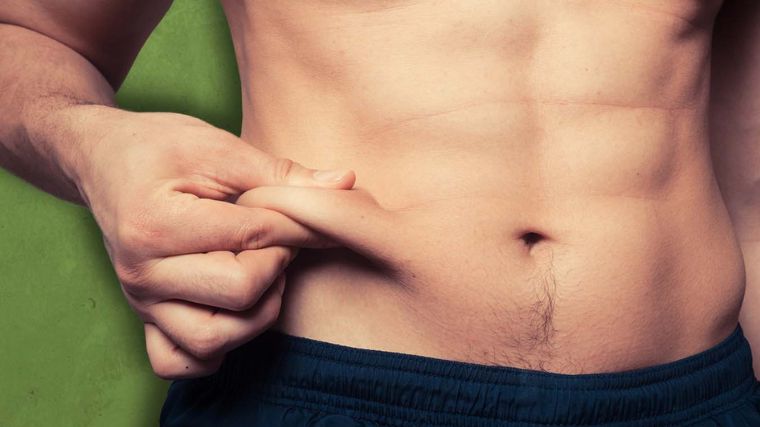 Shirtless man pinching lower abdomen fat