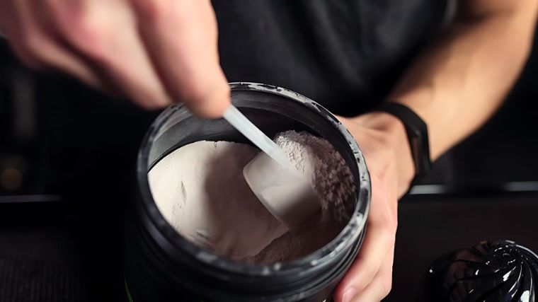 Protein  powder benefits: This photo is of a hand scooping protein powder from a container.