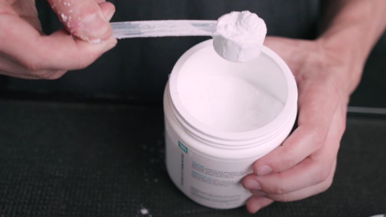 Pros and cons of creatine: An image of a hand holding a scoop of white creatine powder, while the other hand holds the container.