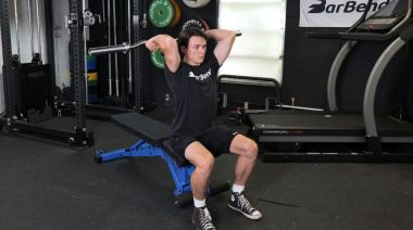A person holding sitting on a weight bench doing the EZ bar French press exercise.