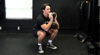 A person doing the goblet squat with a dumbbell.