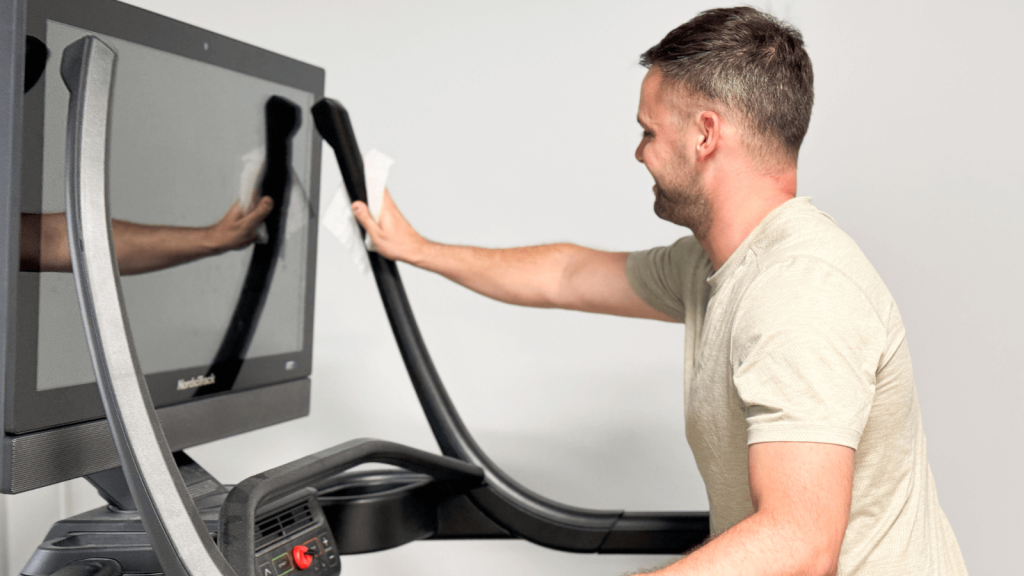 A person cleaning the NordicTrack X32i treadmill handlebars and display.