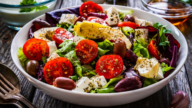 Fresh Greek salad - feta cheese, cherry tomatoes, artichokes, lettuce, black olives and onion on wooden table. for a green Mediterranean diet.