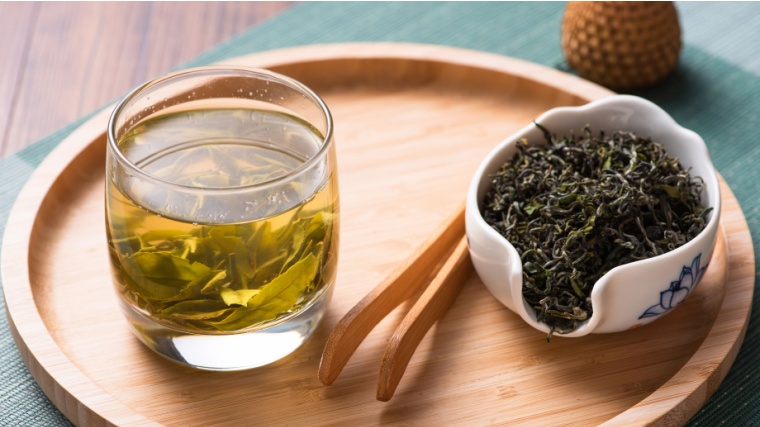 Organic green tea in a glass, beside a small container of dried green tea leaves.
