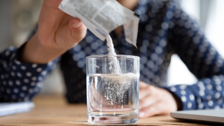 A person pouring a powdered supplement in a glass of water.