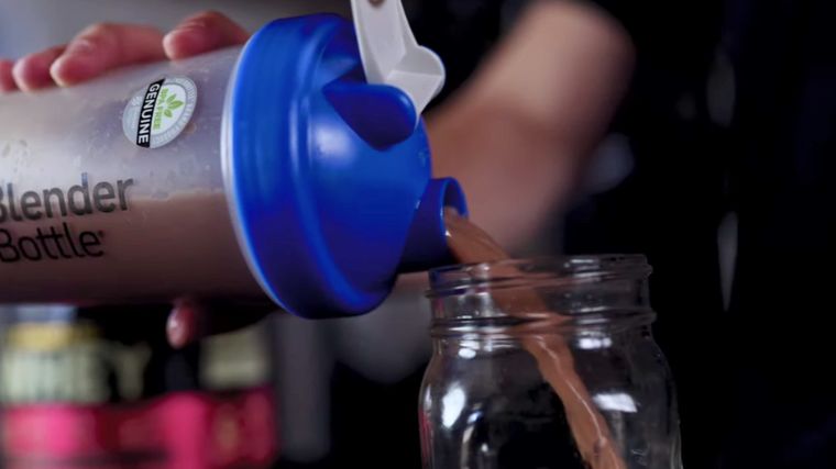 Protein shake being poured out of a shaker bottle into a glass.