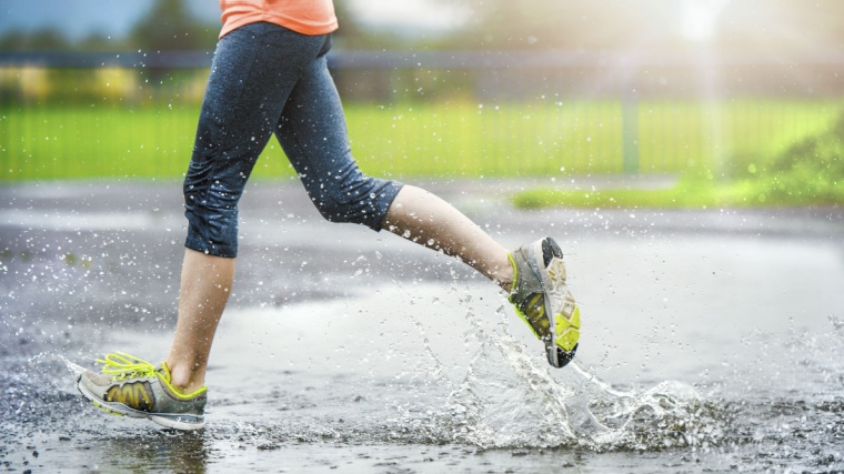 A person running in the rain, stepping into a puddle.