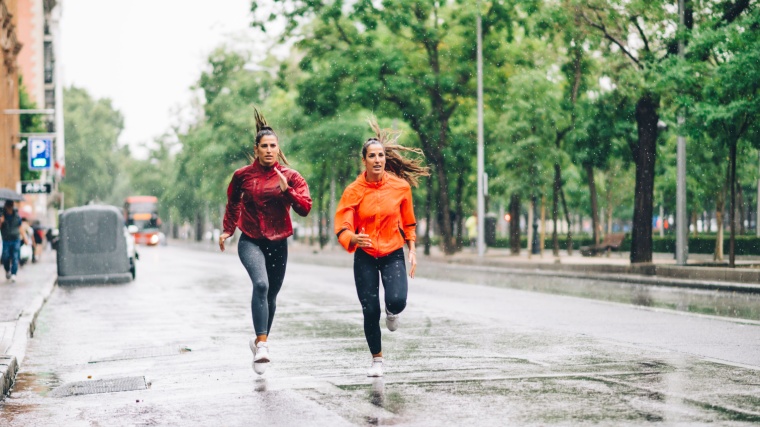 Two people wearing jackets and running the rain.