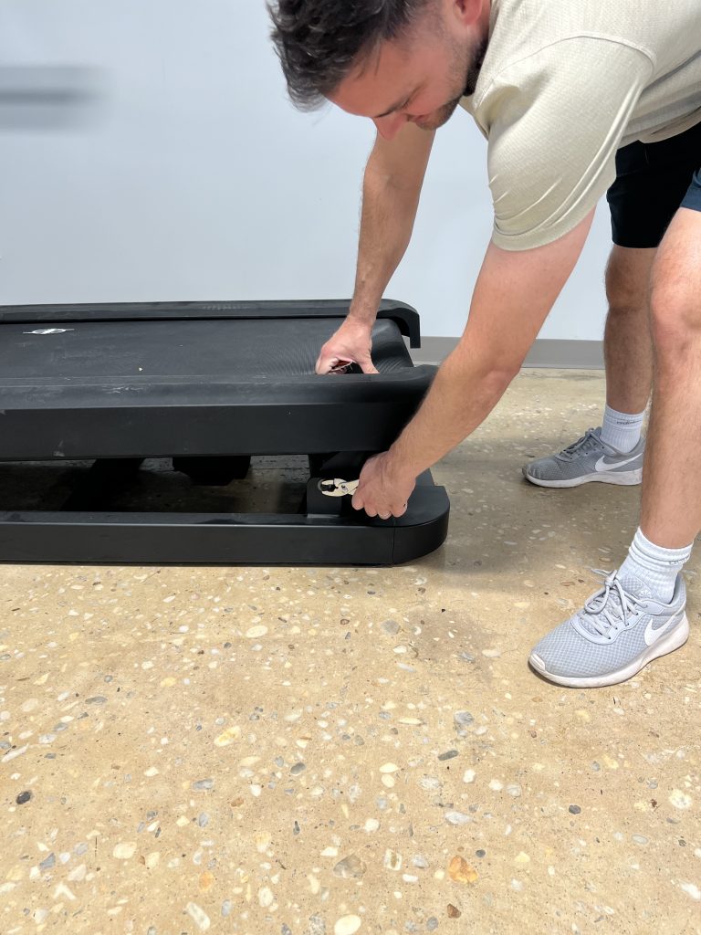 A person adjusting the NordicTrack X32i treadmill deck.