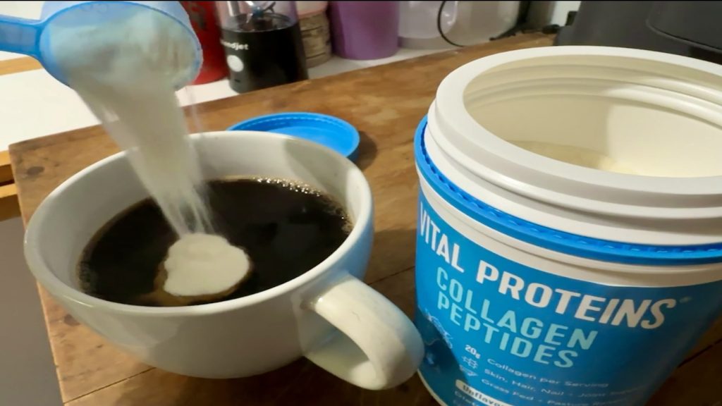 A scoop of Vital Proteins Collagen Peptides is being poured into a cup of coffee.