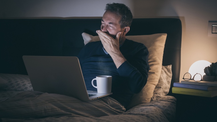A person drinking coffee in his bed feeling sleepy while working.
