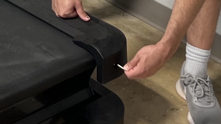 A BarBend tester adjusting the tension of a treadmill belt.