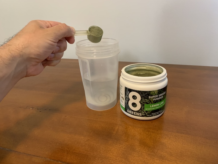 Our tester dumps 8Greens Super Greens Powder into a cup of water.