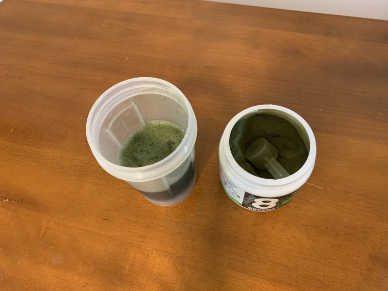 Looking down into a freshly mixed cup and container of 8Greens Super Greens Powder.