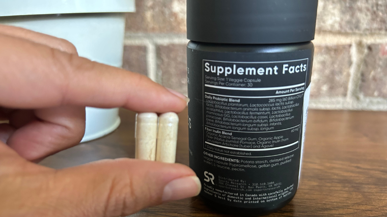 A person holds two Sports Research Probiotics capsules in front of the supplement facts.