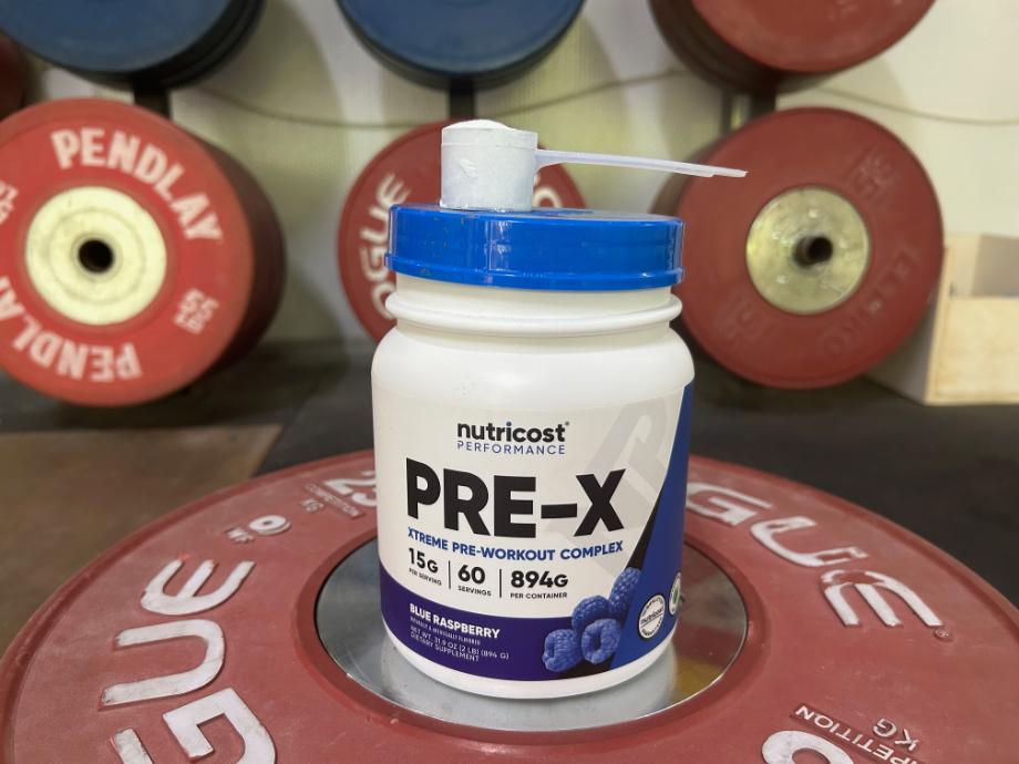 A scoop of Nutricost Pre-Workout is perched with the container on a weight plate.