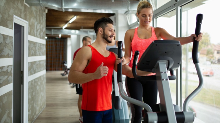 A fit person working out in the gym with the assistance of their personal trainer.