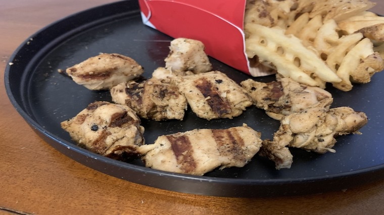 Grilled Chicken Nuggets and fries on a black stoneware plate.