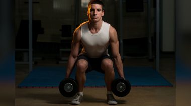 A muscular person performing the dumbbell squat.