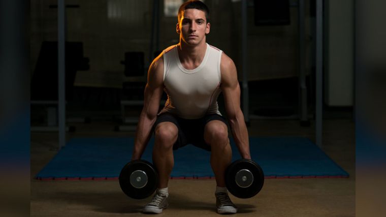 A muscular person performing the dumbbell squat.