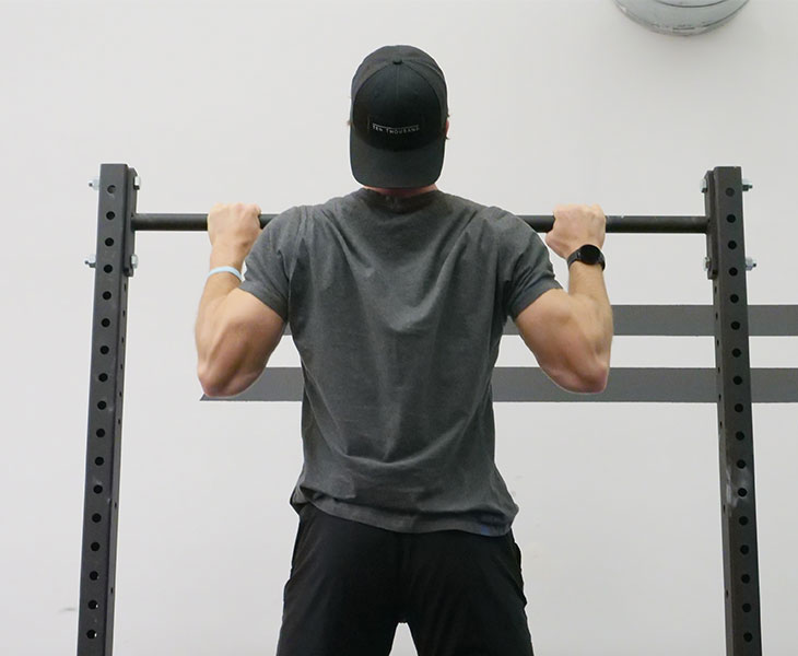 View of a man from behind doing a pull up with his chin above the bar