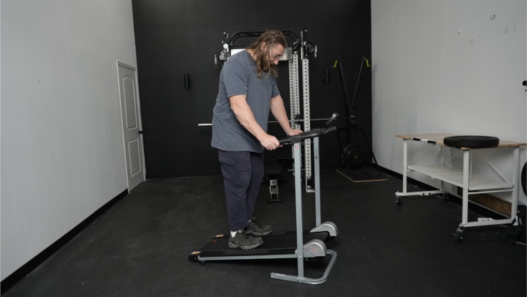 Our tester stands holding the handles on a Sunny Health and Fitness Manual Treadmill.