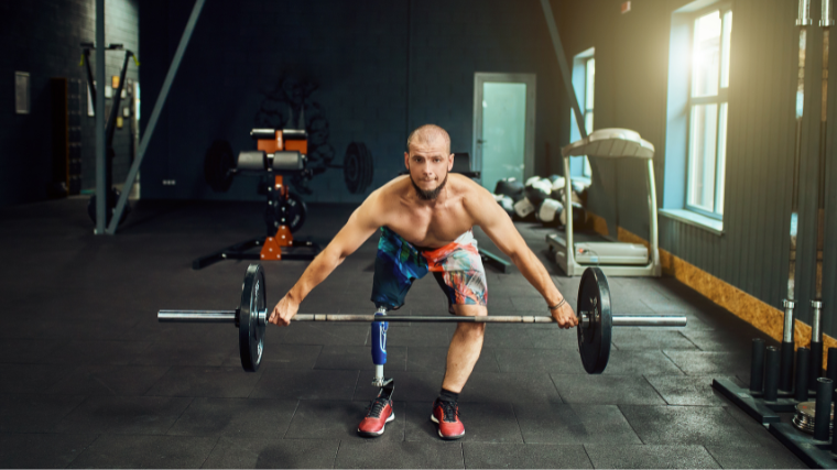 A shirtless athlete with a prosthetic leg performs a snatch with a loaded barbell.