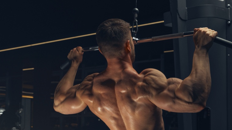 Muscular man performs lat pulldown exercise shirtless