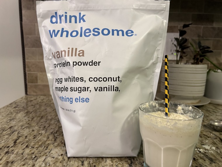 A shake and straw next to a bag of Drink Wholesome Protein Powder