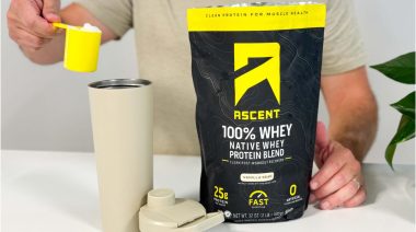 a person holding a scoop of Ascent Whey Protein over a shaker cup