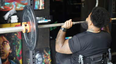 A Black man using a wheelchair presses a loaded barbell overhead.