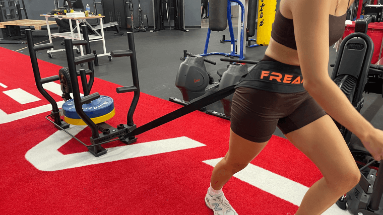 A woman pulls the Freak Athlete Wheelbarrow Sled with a waist belt.