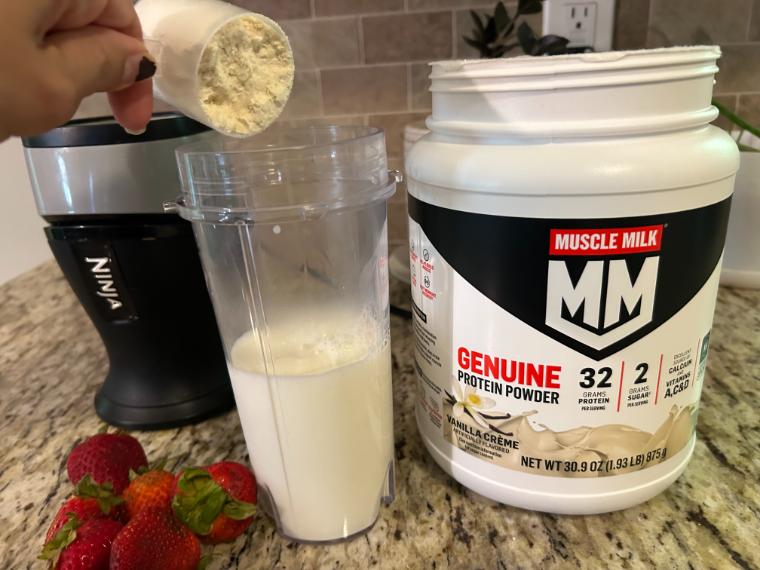 Our tester holding a scoop of Muscle Milk Genuine Protein Powder over their blender cup.