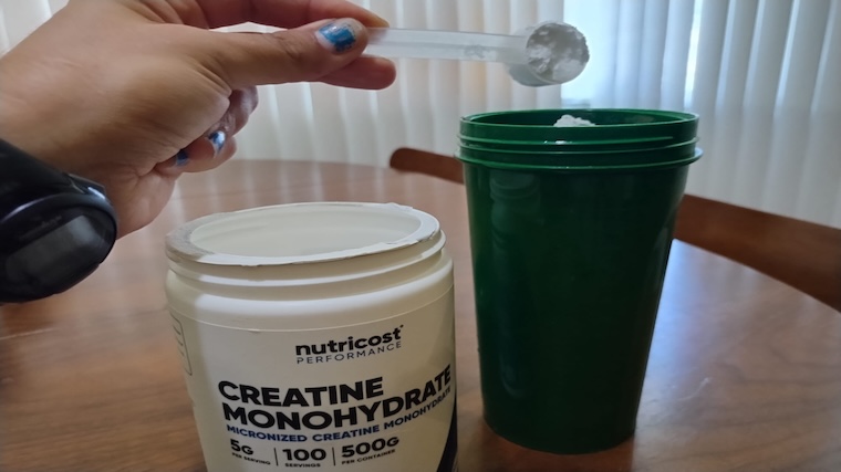 Our tester adding a scoop of Nutricost Creatine to their shaker bottle