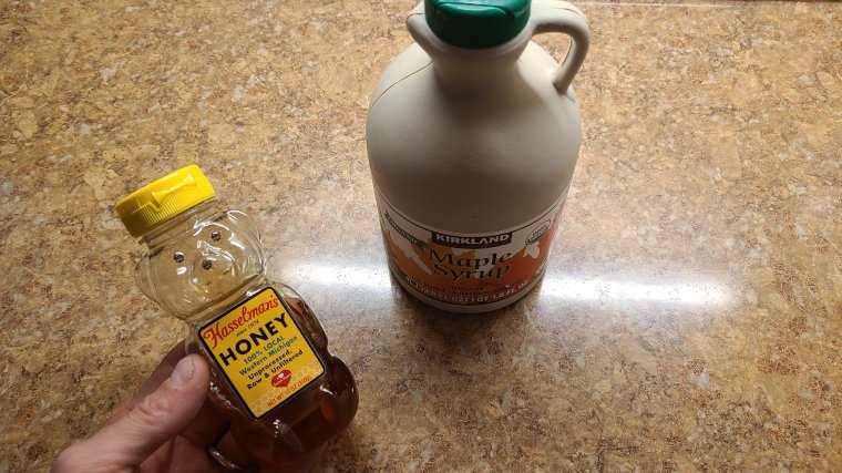 Our tester holding a honey bear next to a jug of maple syrup.