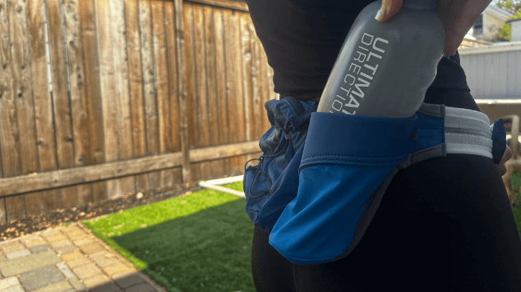 A person tucking a water bottle in the Ultimate Direction Mountain Belt.