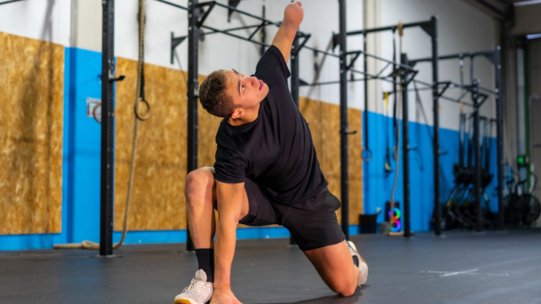 An athlete performs a stretch on a yoga mat in the gym.