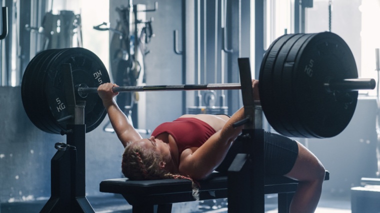 Woman performs bench press with arched back