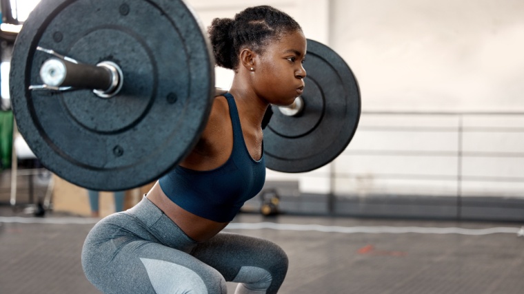 African-American woman performs back squats in functional training gym