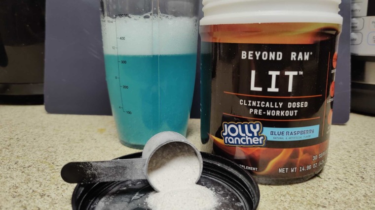 A cup of LIT Pre-Workout next to the scoop and container