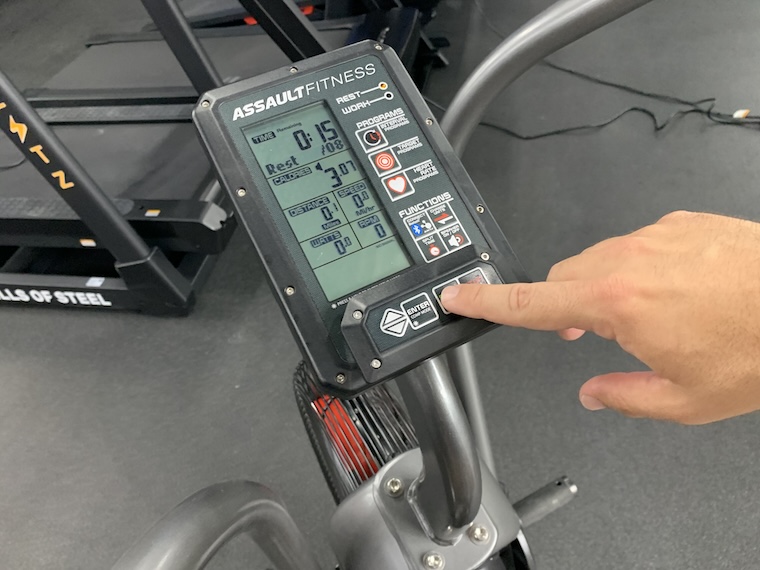 a person adjusting the LCD display of the Assault Fitness AirBike Elite.