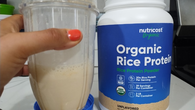 Our tester holds up a Nutricost Organic Rice Protein shake next to the container