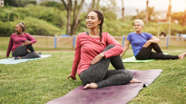 A multiracial, multigenerational group of people practice yoga in a park.