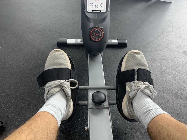 Two feet secured in the foot straps of the Sunny Health & Fitness SF-RW5801 Rowing Machine.