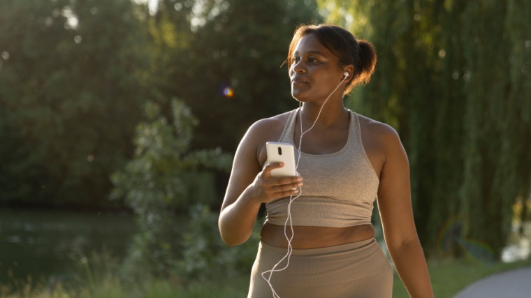 Woman walks outdoors with iphone and wired earbuds