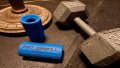 A dumbbell sits next to a pair of grip strengtheners that have been staged for the Fat Gripz Review featured image