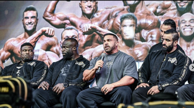 2023 Mr. Olympia Derek Lunsford speaking on stage with fellow competitors.